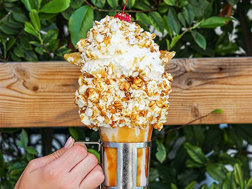 Close up of a hand holding the Peanut Brittle Cracker Jack Shake from our milkshake bar near Color Factory, NYC.