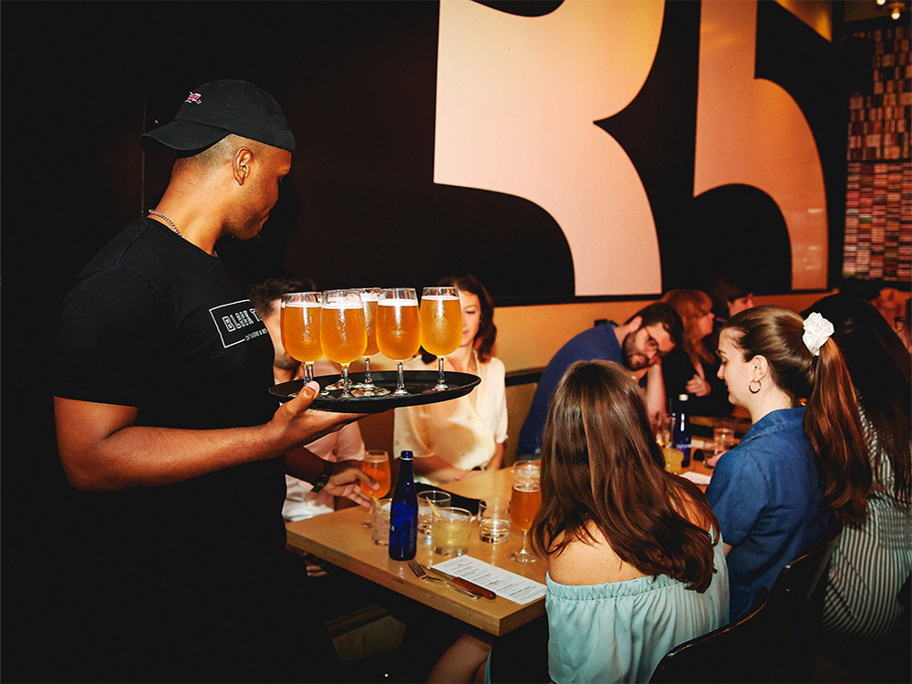 Black Tap employee bringing a tray of beers to a table with customers at our birthday party place near Theater District, NYC.
