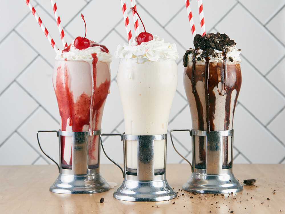 A Strawberry Milkshake, Vanilla Milkshake, and Chocolate Milkshake with cookies on top, frequently ordered for Bowery restaurant food delivery service.