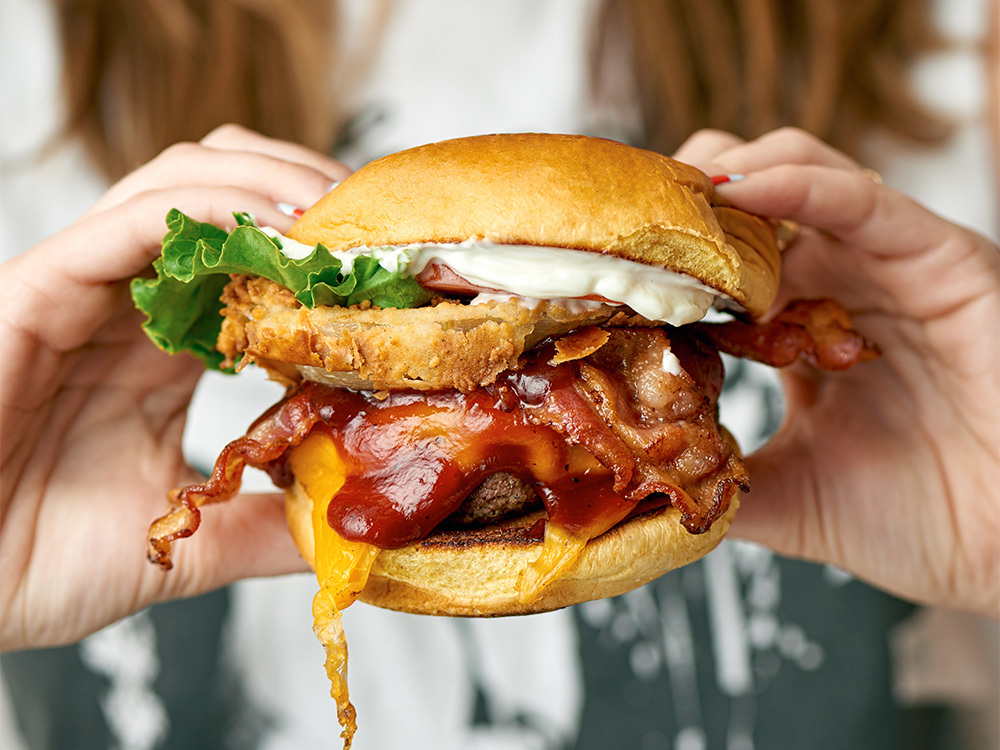 Close up view of a woman holding our Texan Burger, a popular choice for food delivery near Hudson Yards, New York City.