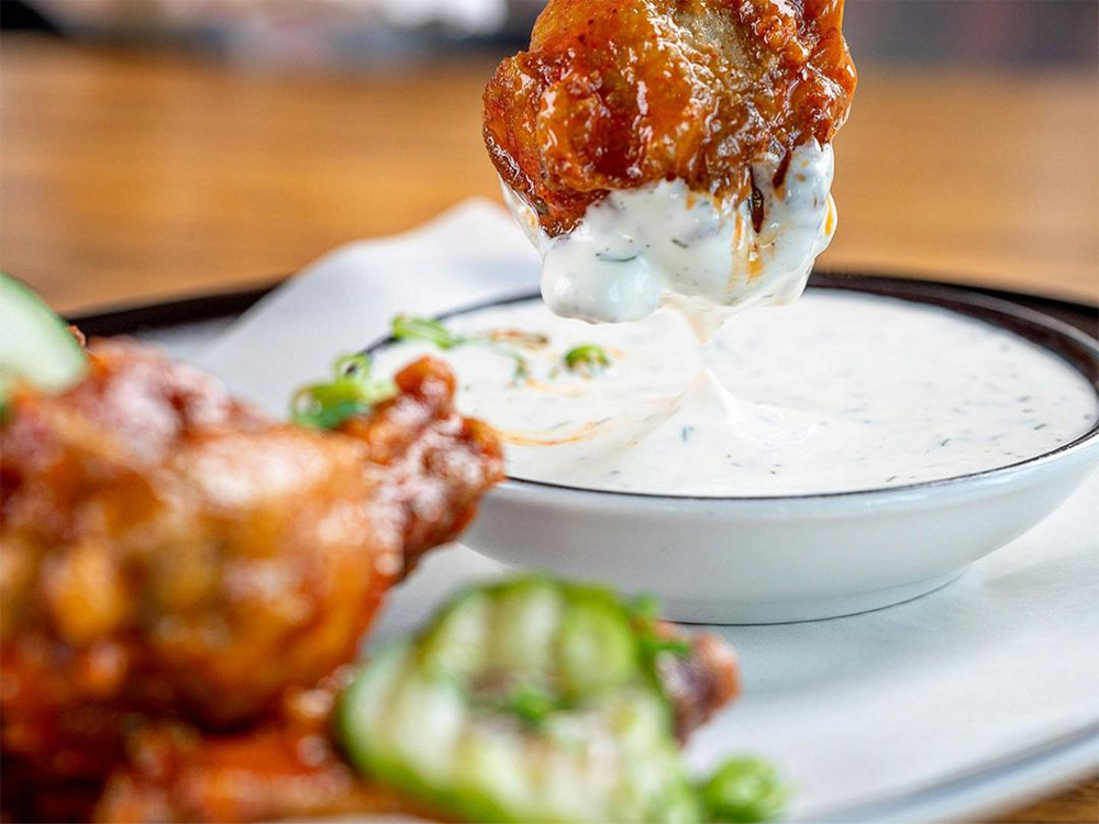 Nashville Hot Wings being dipped in House Buttermilk-Dill, a go-to for wings delivery near Broadway, NYC.