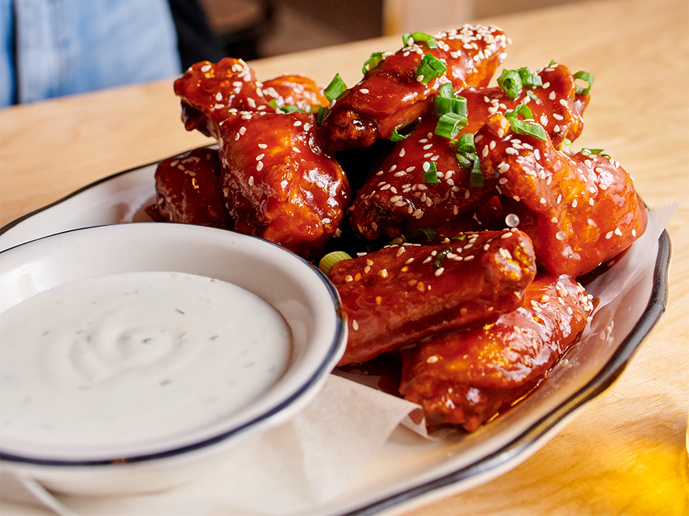 Close up view of our Korean BBQ Wings with side of House Buttermilk-Dill, a popular option for our wings delivery near Hell's Kitchen, New York City.