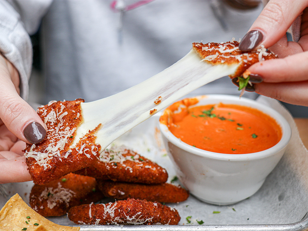 Close view of a woman pulling apart our Fried Mozz starter, a go-to for meal delivery near Batman Building, Nashville.