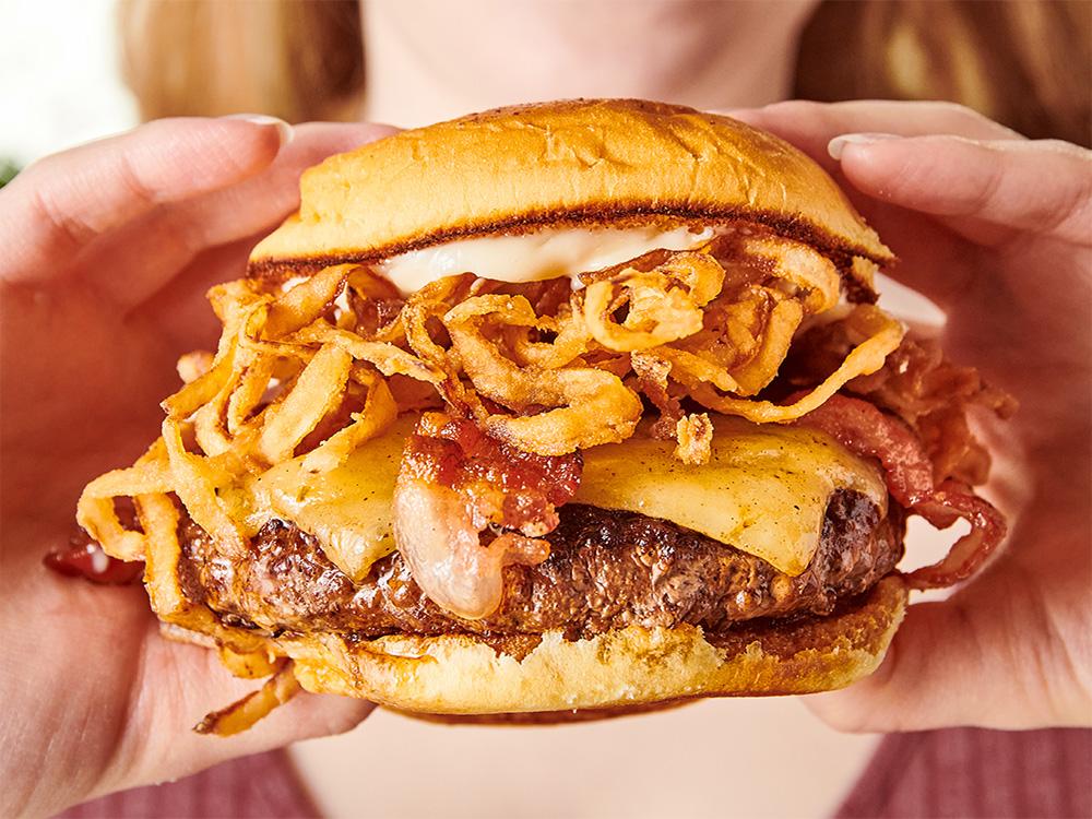 Close up view of hands holding the Wagyu Steakhouse Burger, a top Alphabet City wagyu burger.