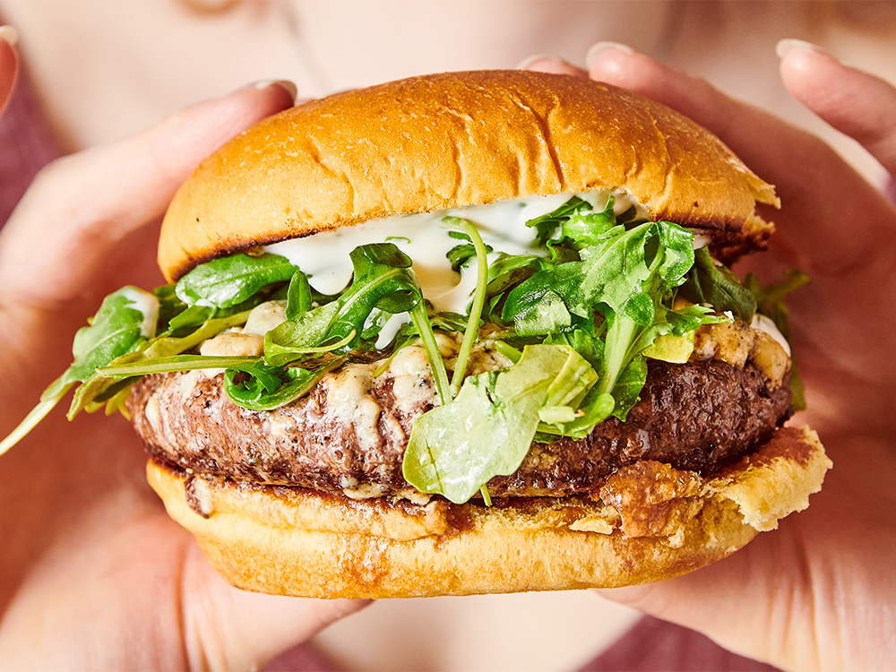 Close up view of hands holding The Champ, one of our gourmet craft wagyu burgers near Broadway, NYC.