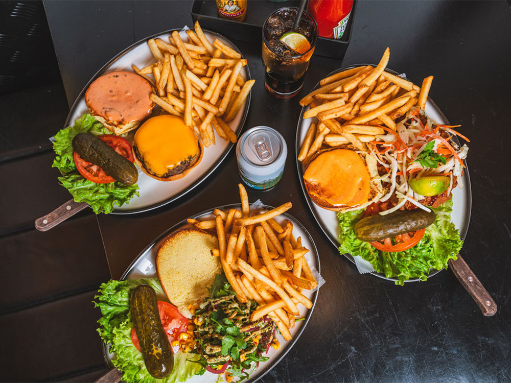 Three burgers opened on plates next to drinks at our burger restaurant near Bow, London, United Kingdom.